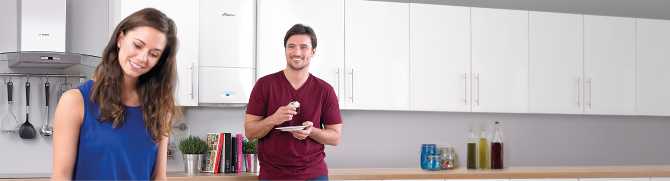 Photo of a couple in a kitchen where a man is eating a cupcake with a grin on his face.
